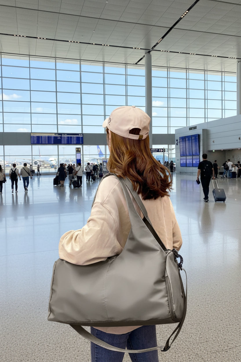 A person carrying a large gray Oxford cloth waterproof travel bag over their shoulder.